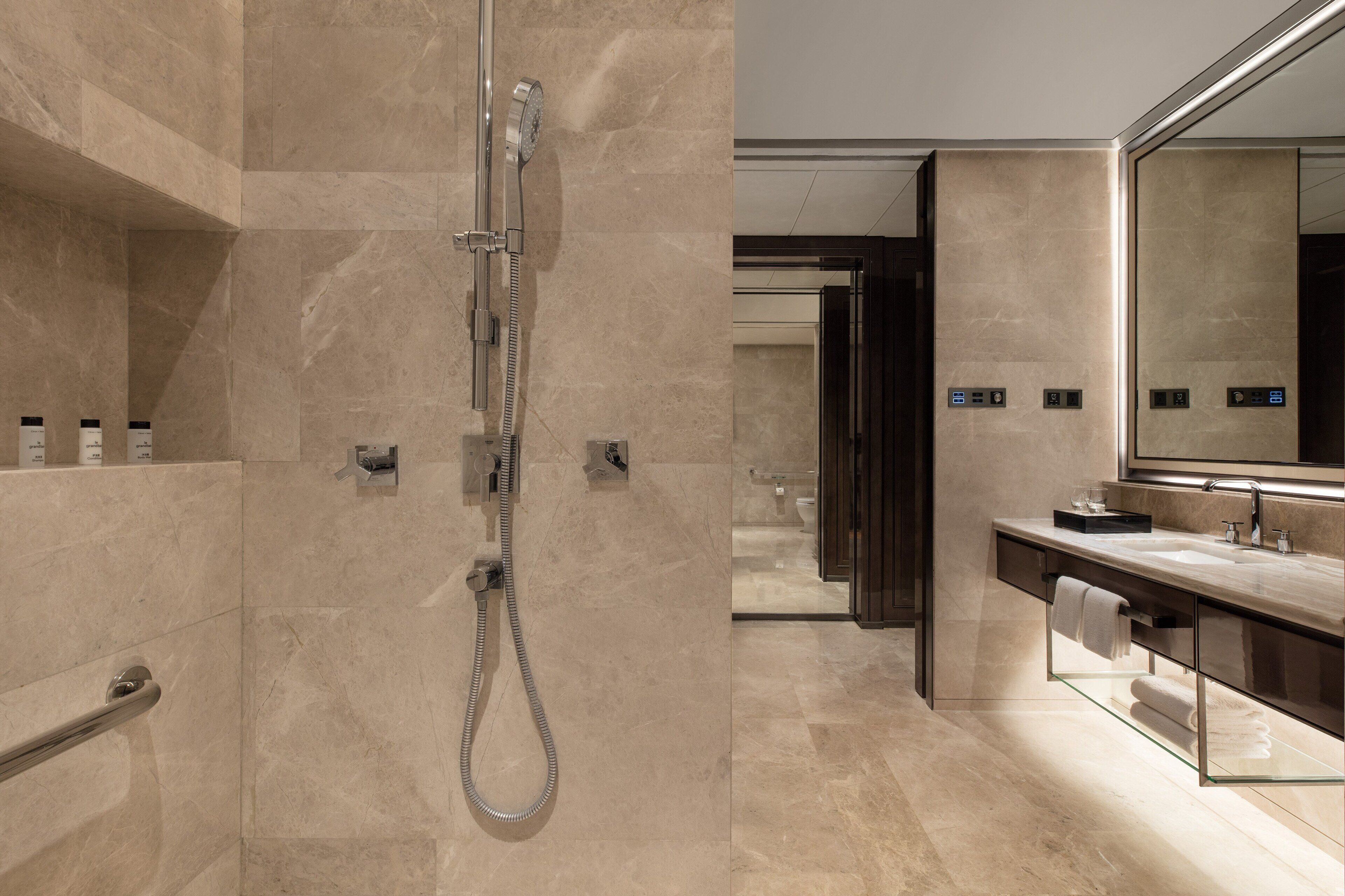 Une salle de bain moderne dotée d’une douche en verre, d’un grand miroir et d’un sol carrelé en marbre.