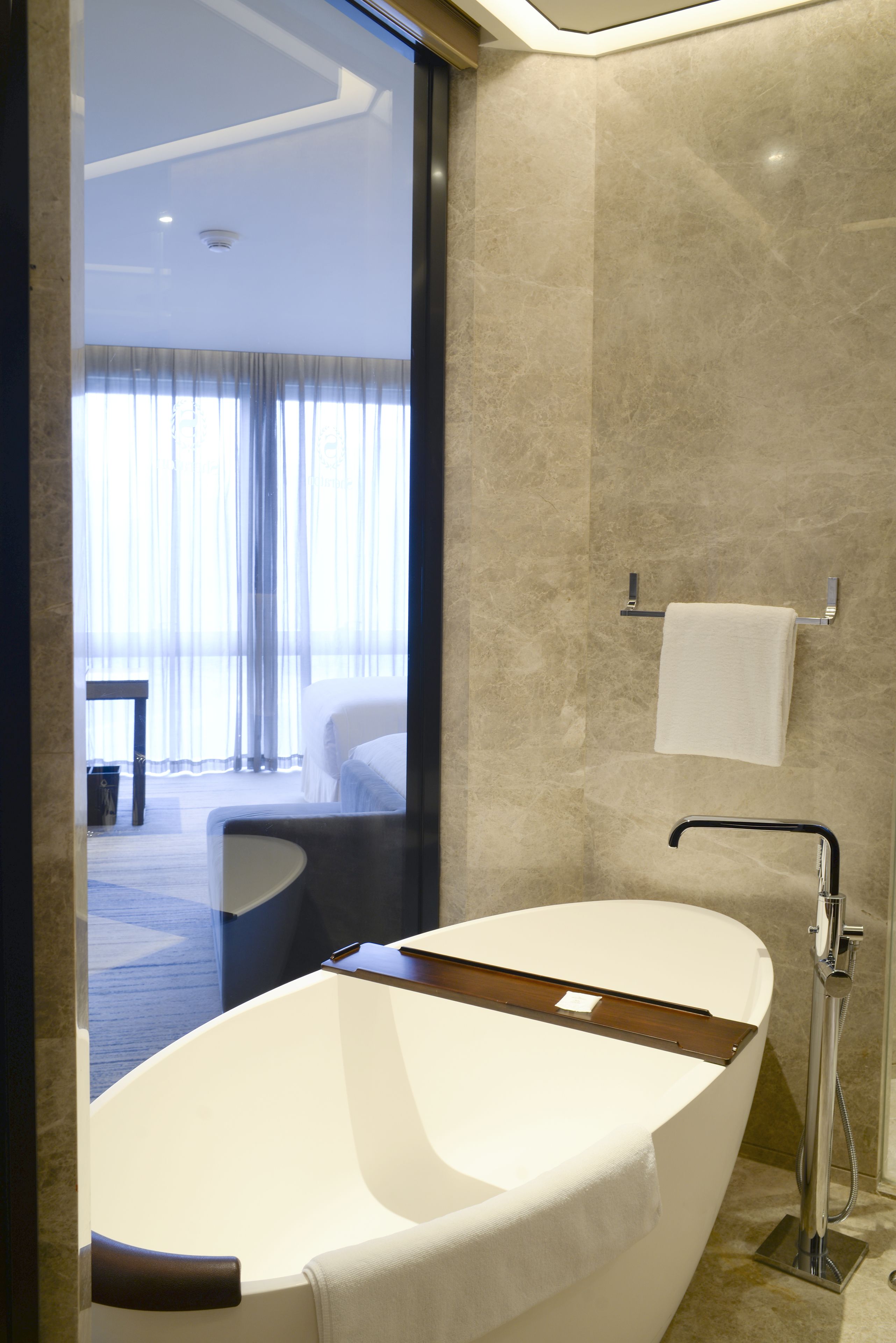 A modern bathroom with a freestanding bathtub, a towel rack, and a visible window with curtains.
