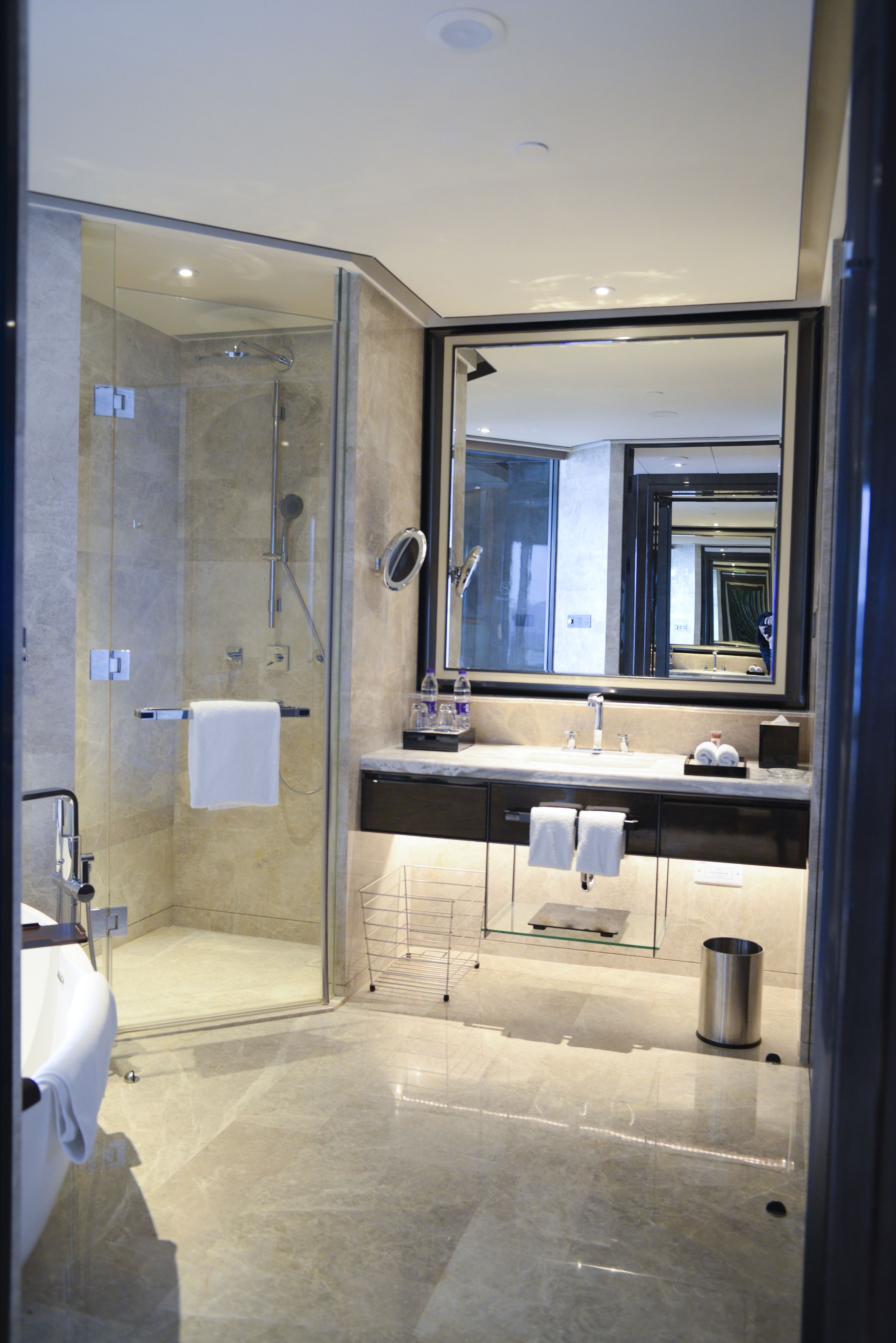 A modern bathroom with a glass-enclosed shower, a large mirror, and a marble-topped sink.