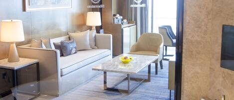 A modern hotel room with a large bathtub, a sofa, a coffee table, and a dining area.