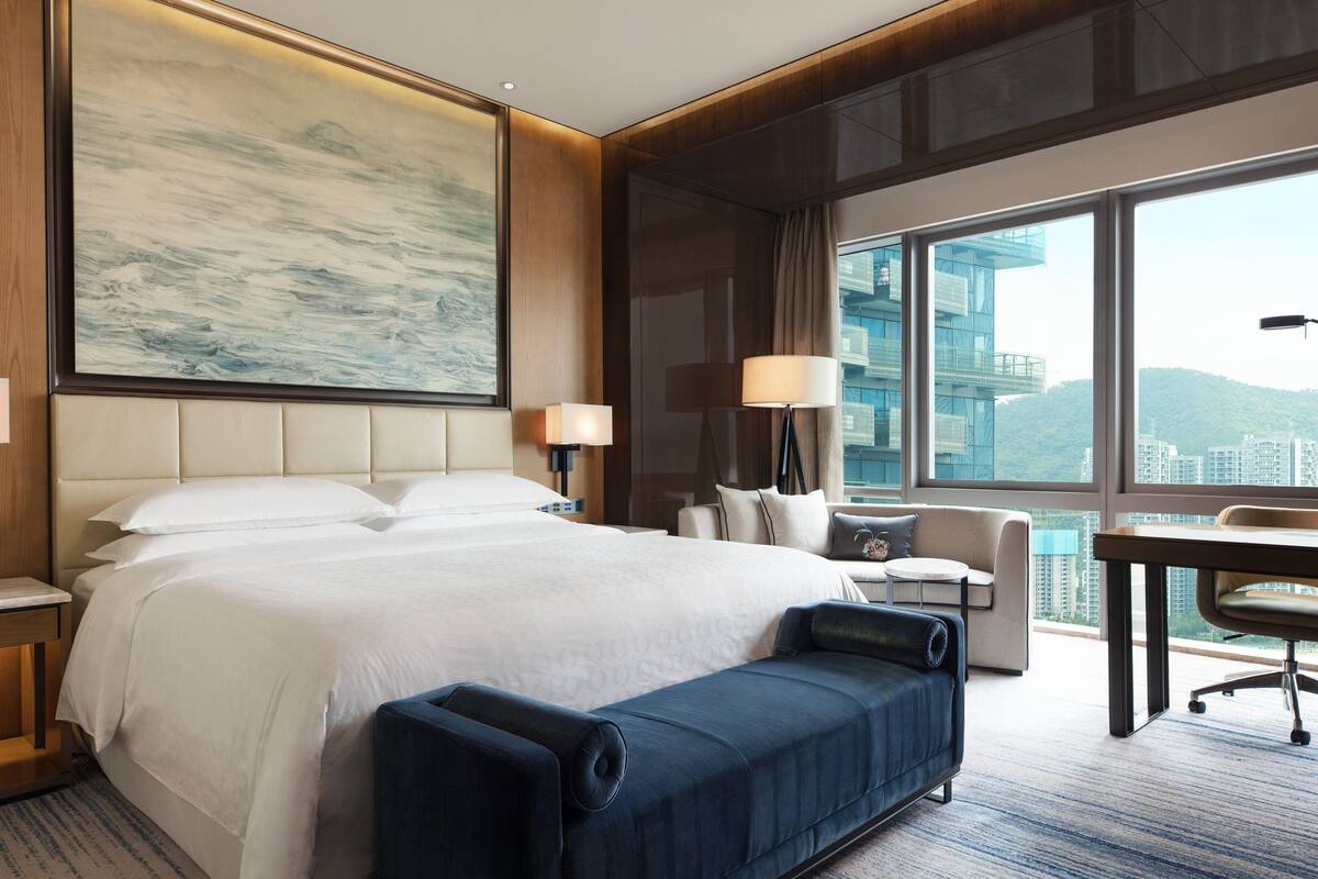 Ein Hotelzimmer mit einem großen Bett, einem Schreibtisch, einem Stuhl und Blick auf die Stadt.