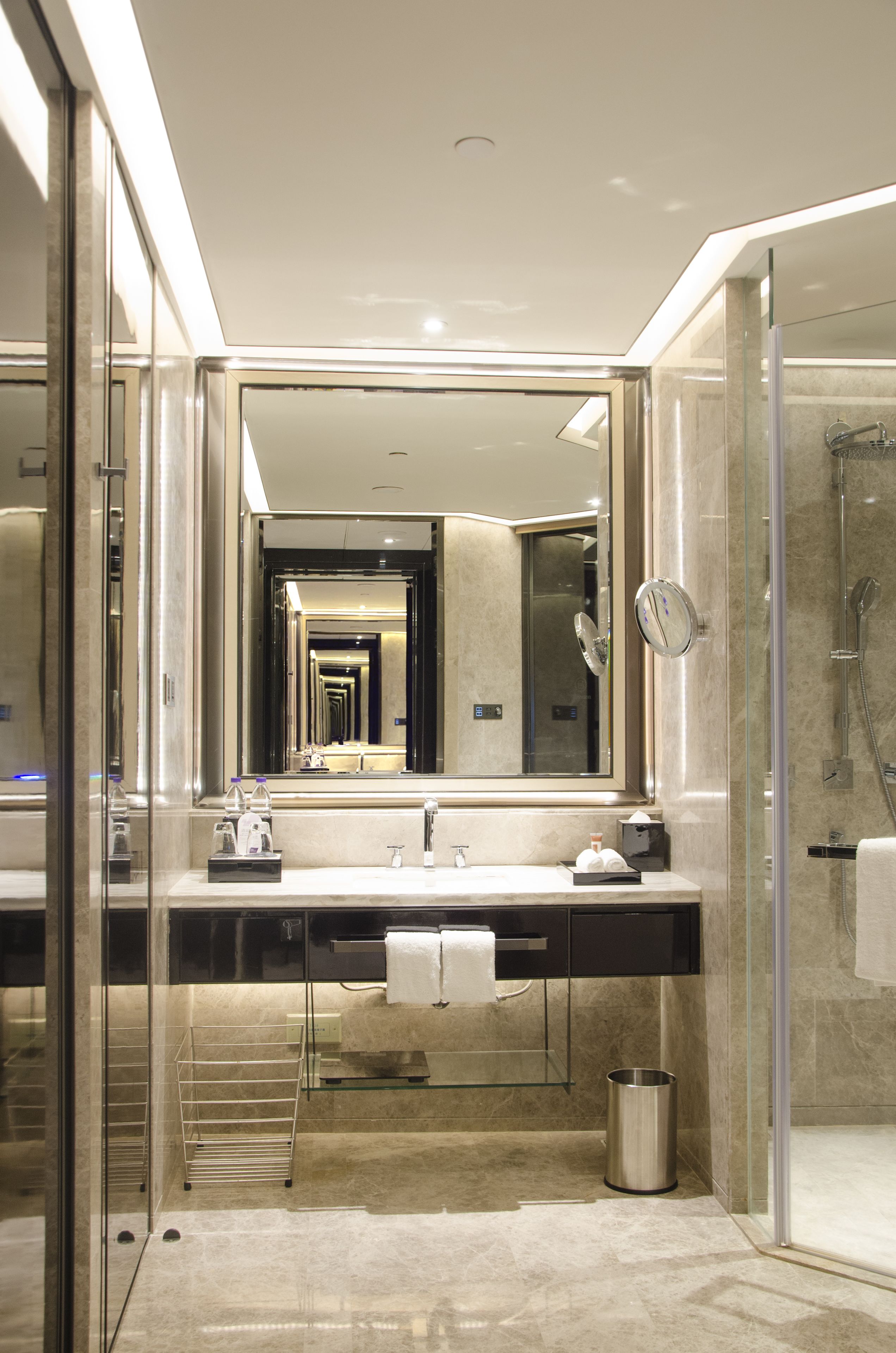 Un baño moderno con un espejo grande, cabina de ducha con paredes de cristal y suelo de baldosas de mármol.