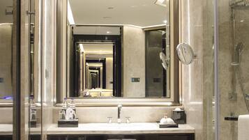 Un baño moderno con un espejo grande, cabina de ducha con paredes de cristal y suelo de baldosas de mármol.