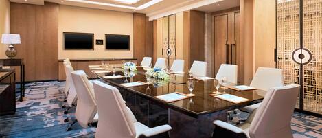 A conference room with a long table, white chairs, a TV, and a decorative screen.