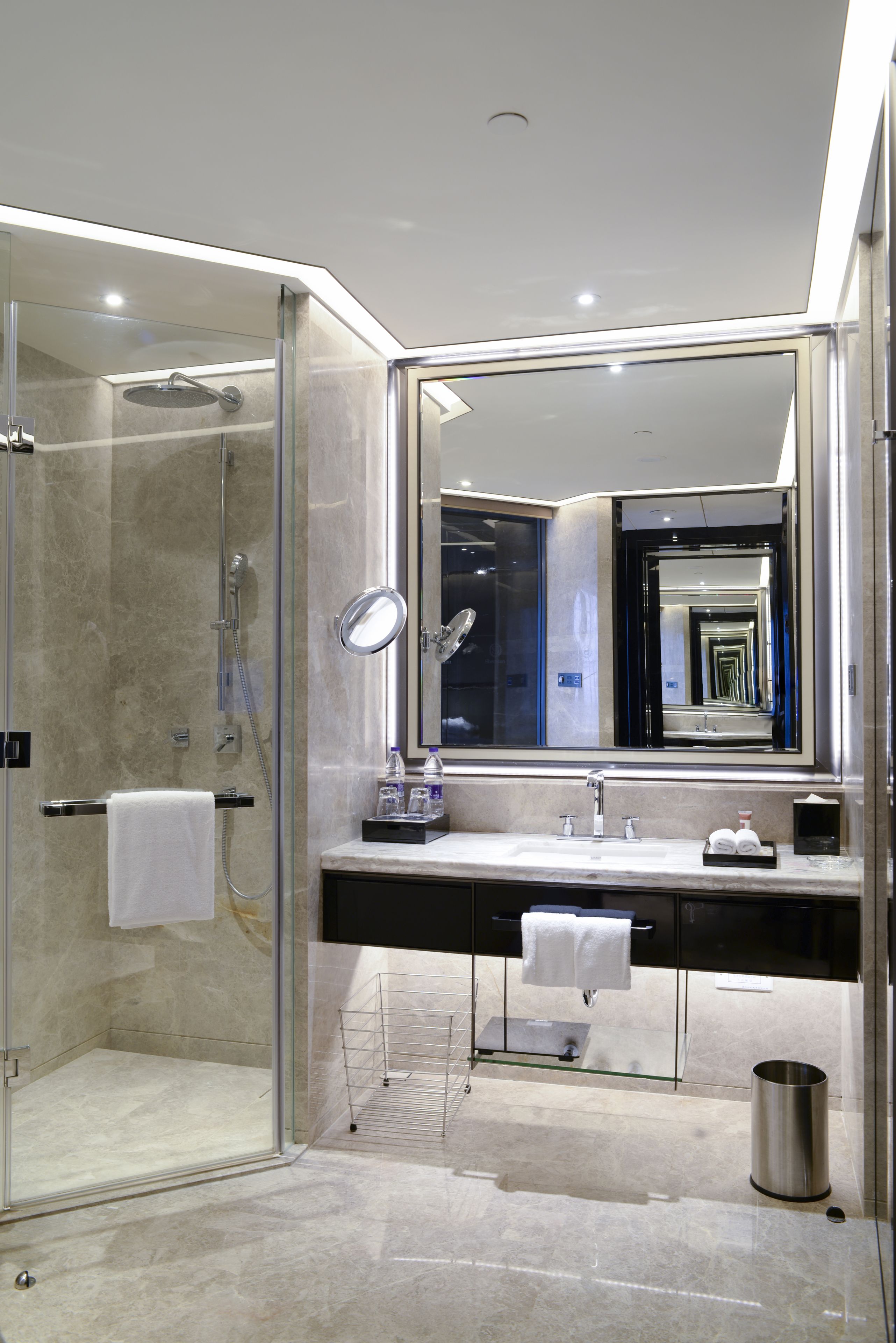 Een moderne badkamer met een douchecabine van glas, een grote spiegel en een marmeren aanrechtblad.