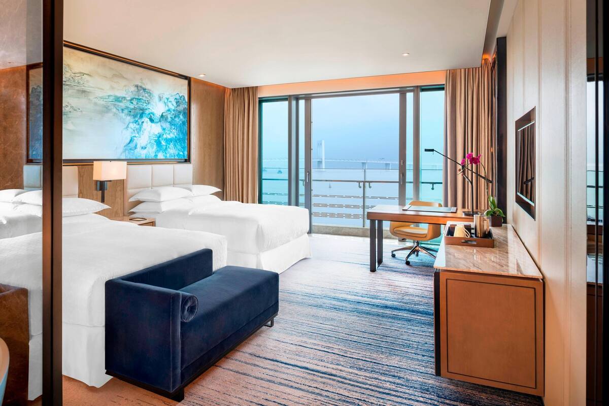 Ein Hotelzimmer mit einem großen Bett, einem Schreibtisch, einem Sessel und Meerblick.