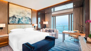 Quarto de hotel com uma cama grande, uma escrivaninha, um sofá e vista para o oceano.