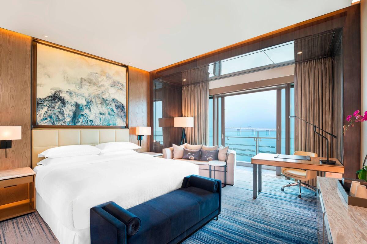 Ein Hotelzimmer mit einem großen Bett, einem Schreibtisch, einer Sitzecke und Blick auf den Ozean.