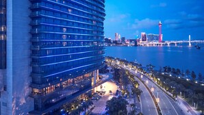 Um hotel moderno com fachada curva, uma torre imponente e vista para uma ponte e horizonte urbano.