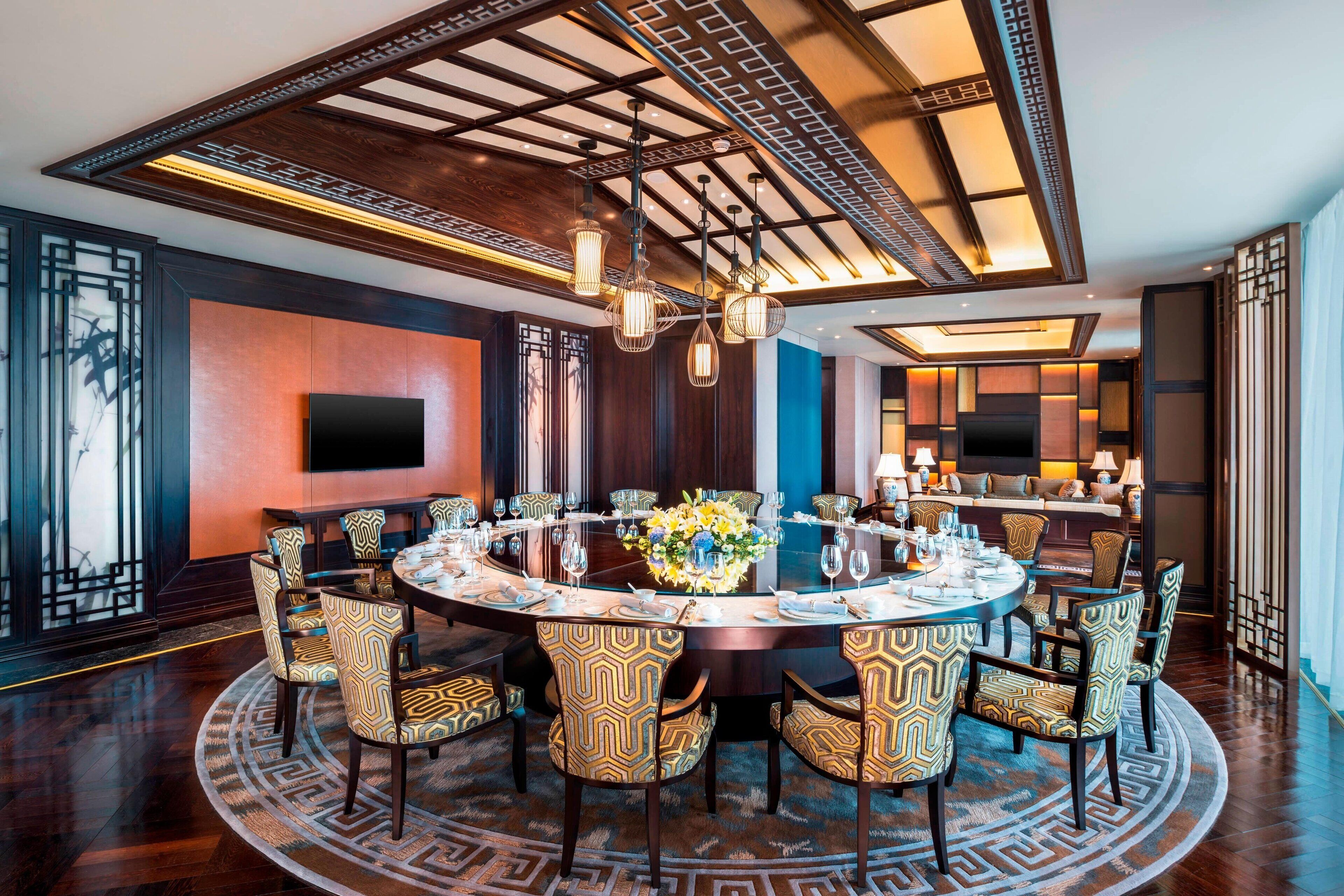 A round dining table with patterned chairs, a central floral arrangement, and a modern chandelier.