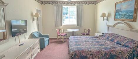 Habitación de hotel con cama, escritorio, silla, televisor y ventana con cortinas.