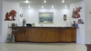 A reception desk with a wooden finish, a framed painting of a beach scene, and decorative animal figures. - Lighthouse Inn (Crescent City)