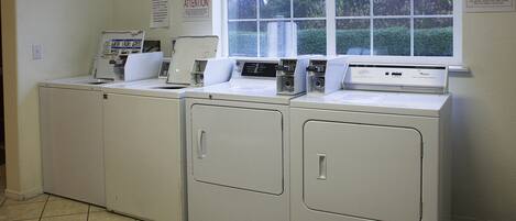 A laundry area with four white washers and dryers, a window with a view of greenery, and an attention sign on the wall.