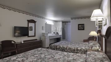 Ett hotellrum med två sängar, ett skrivbord, en tv, en spegel, en lampa och en dörr.