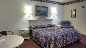 A hotel room with a bed, a desk, a chair, and a painting on the wall. - Lighthouse Inn (Crescent City)