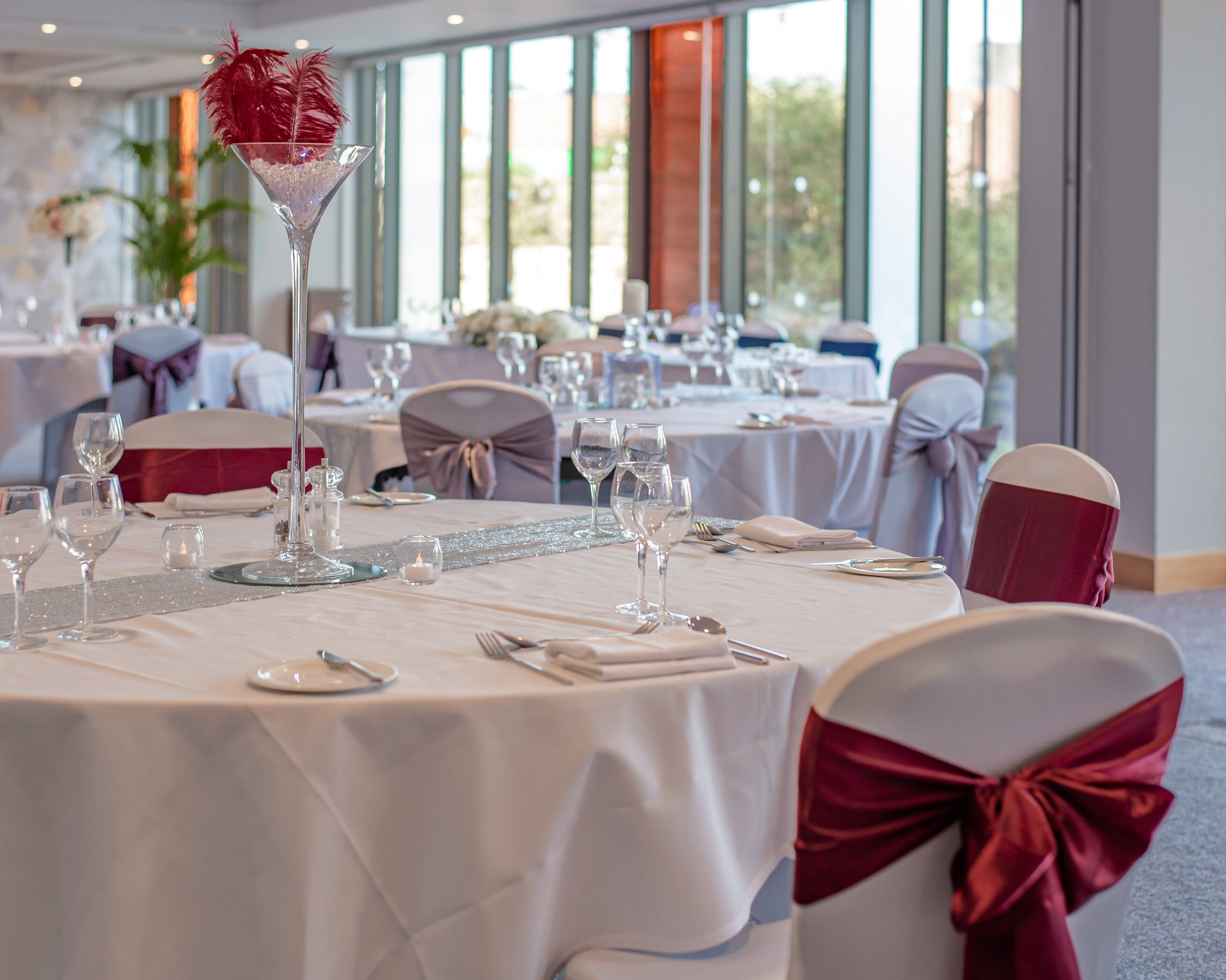 A banquet hall with round tables set for a formal event, featuring white tablecloths and red chair sashes.