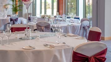 A banquet hall with round tables set for a formal event, featuring white tablecloths and red chair sashes.