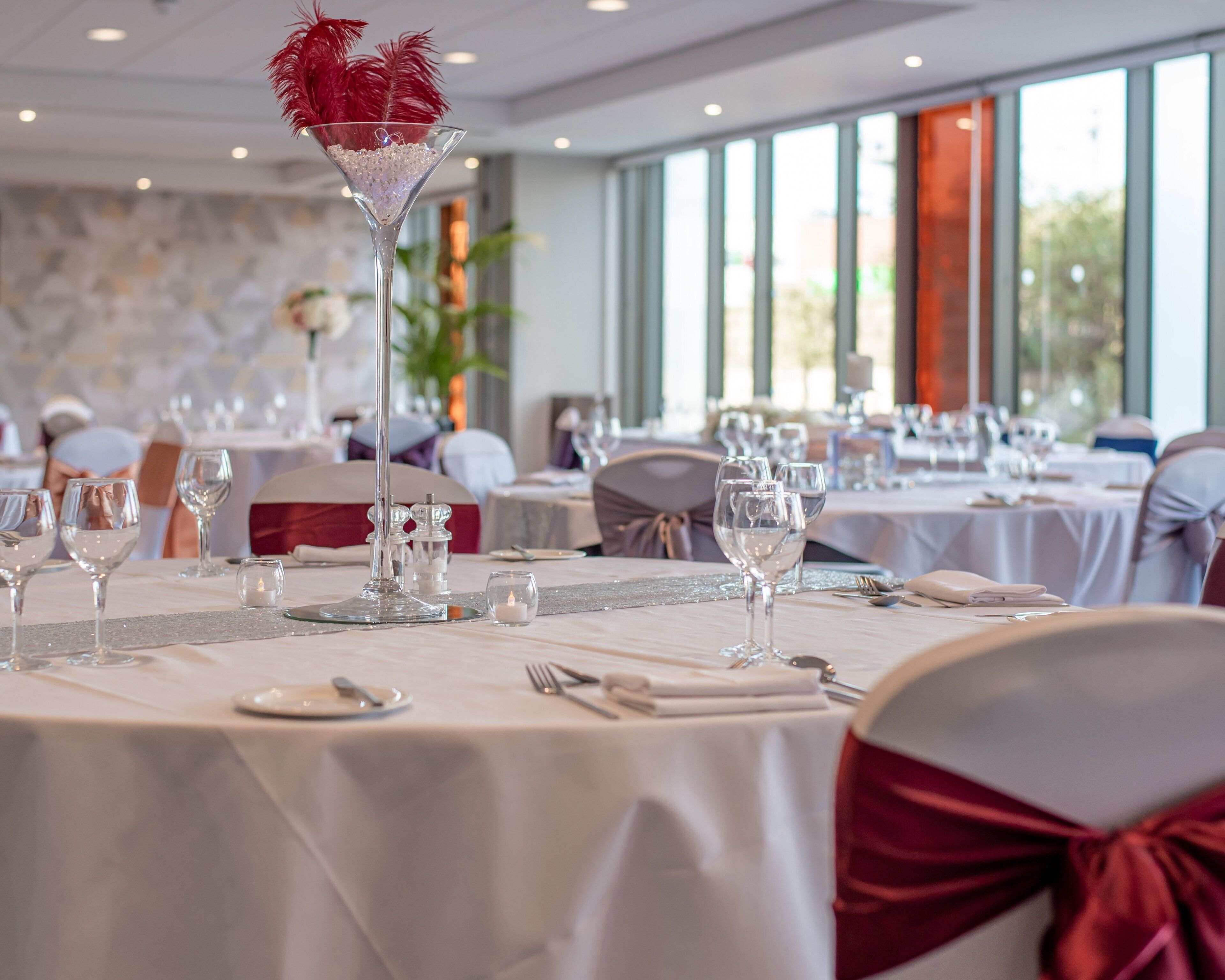 Een balzaal met ronde tafels gedekt voor een formeel evenement, met helder glaswerk en elegante tafeldecoraties.