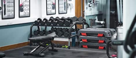 A gym with weightlifting equipment, mirrors, and a clock on the wall.