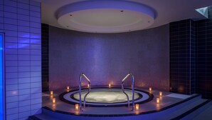 A modern spa with a circular hot tub, steps leading up to it, and candles providing ambient lighting.