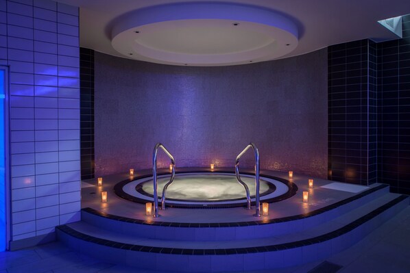 Un spa moderno con una bañera de hidromasaje circular, escalones que la conducen y velas que crean una iluminación ambiental.