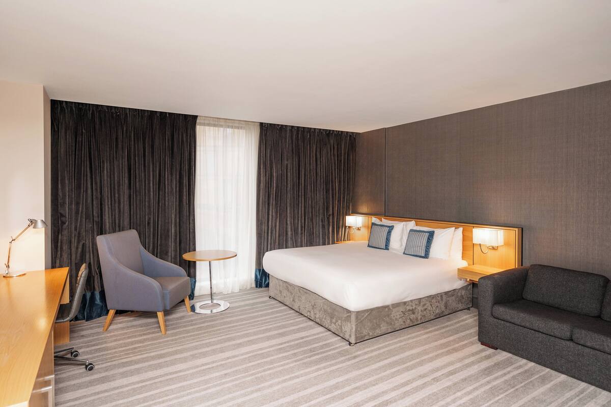 A hotel room with a large bed, a desk, a chair, and a small round table.