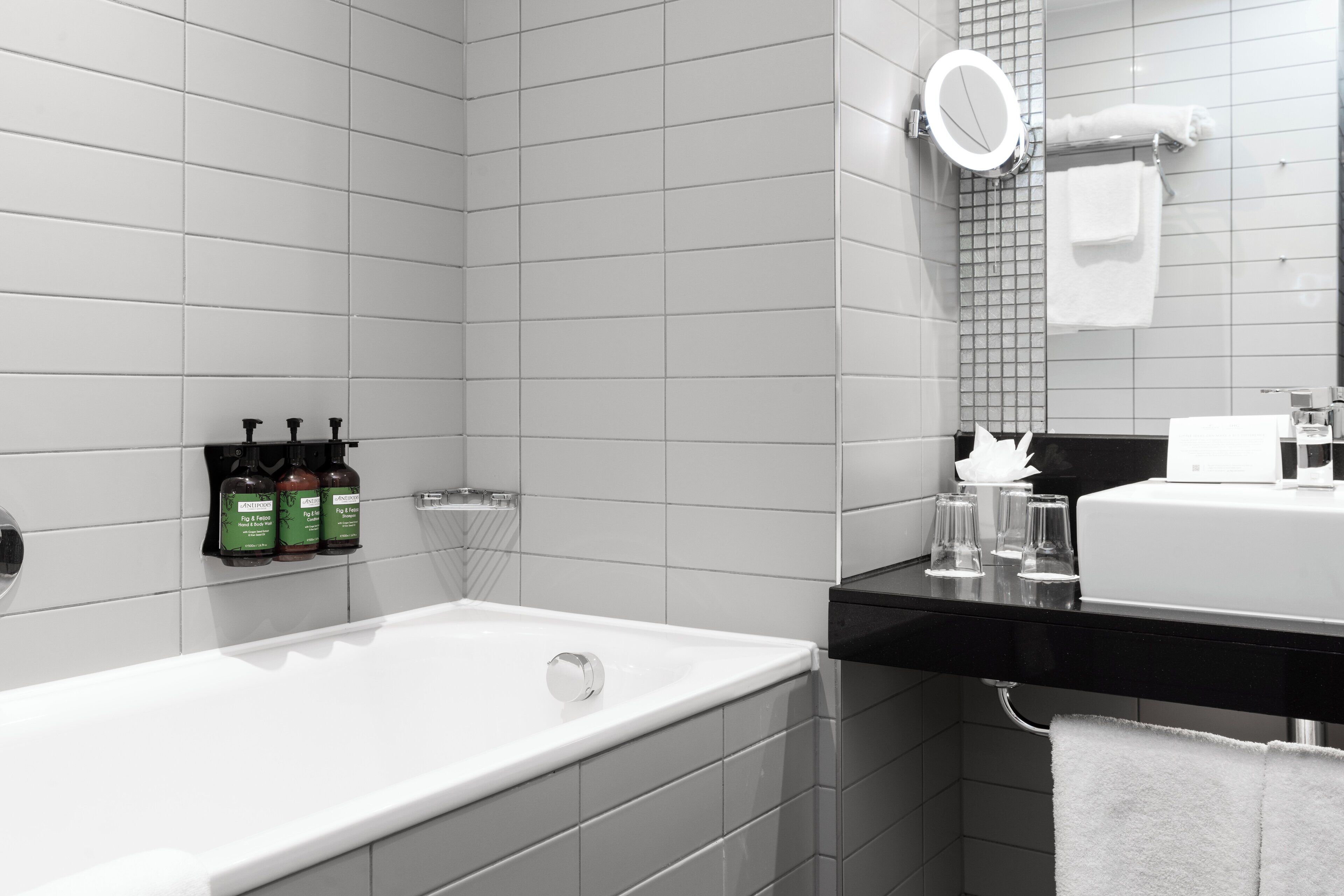 A modern bathroom with a white bathtub, a black countertop, and a mirror above the sink. There are three bottles of shampoo on the wall.
