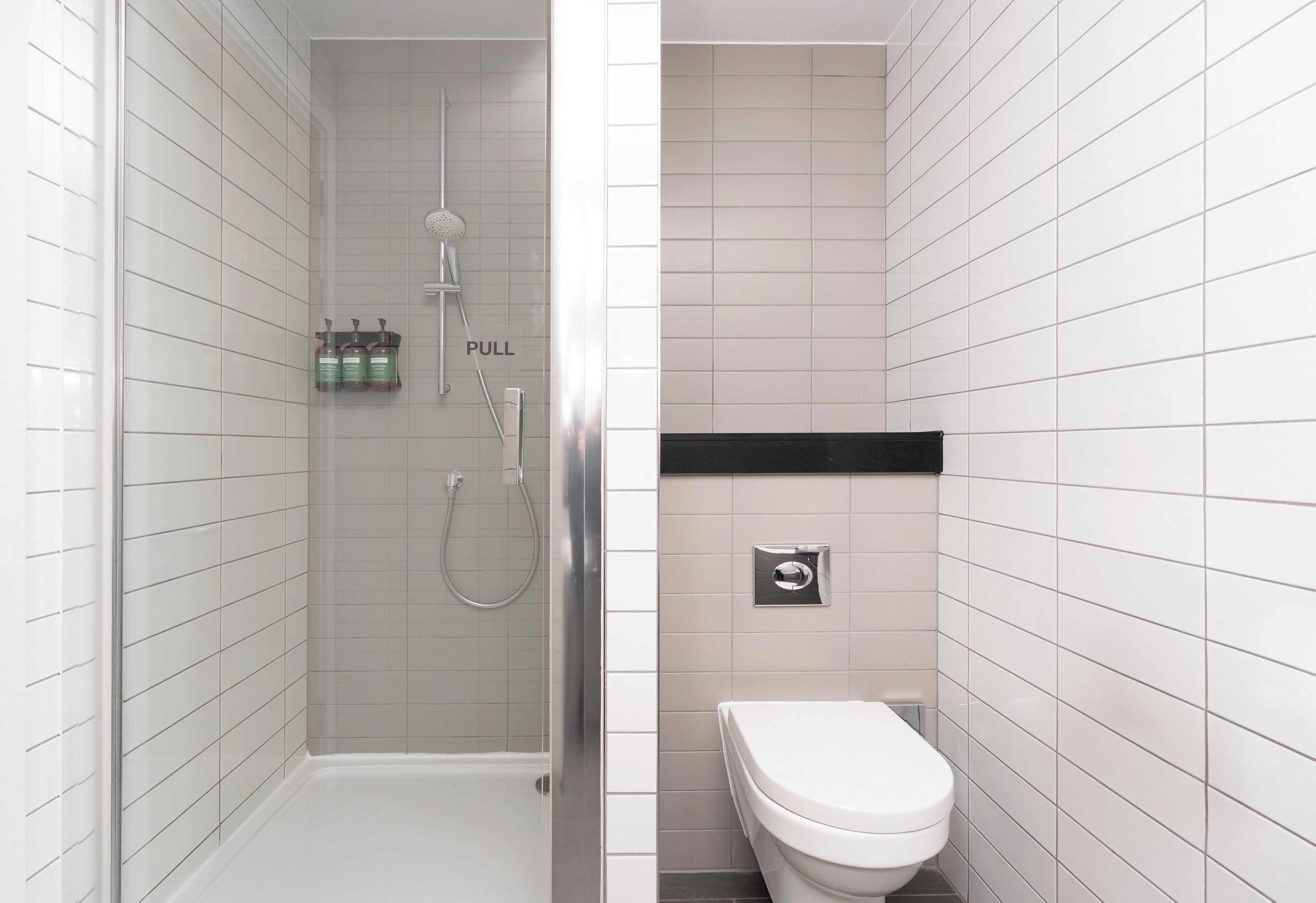 A modern bathroom with a glass-enclosed shower, a toilet, and a shelf with toiletries.