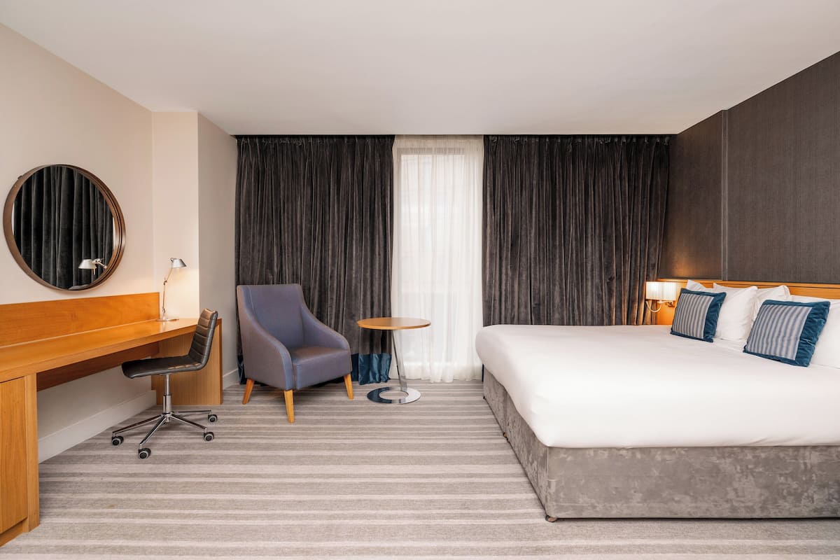A hotel room with a large bed, a desk, a chair, a small round table, and a large mirror.