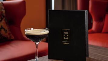A cocktail glass on a wooden table with a black menu stand labeled "The Gin Bar Menu".