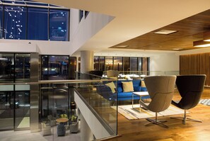 Een modern interieur met een glazen balustrade, een blauwe bank en een hoog plafond met houten balken.