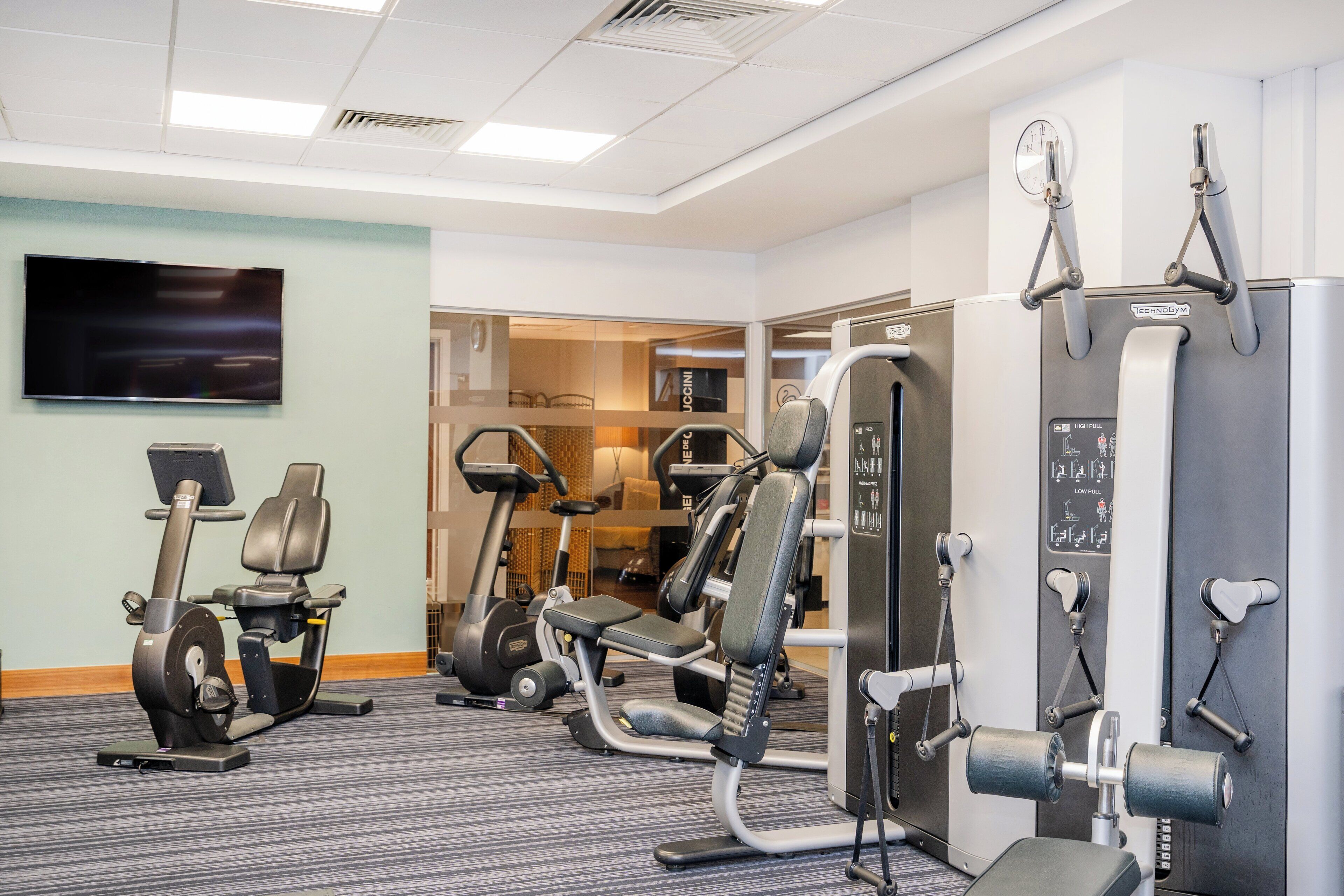 Une salle de sport équipée de machines de cardio, d’appareils de musculation et d’un téléviseur fixé au mur.