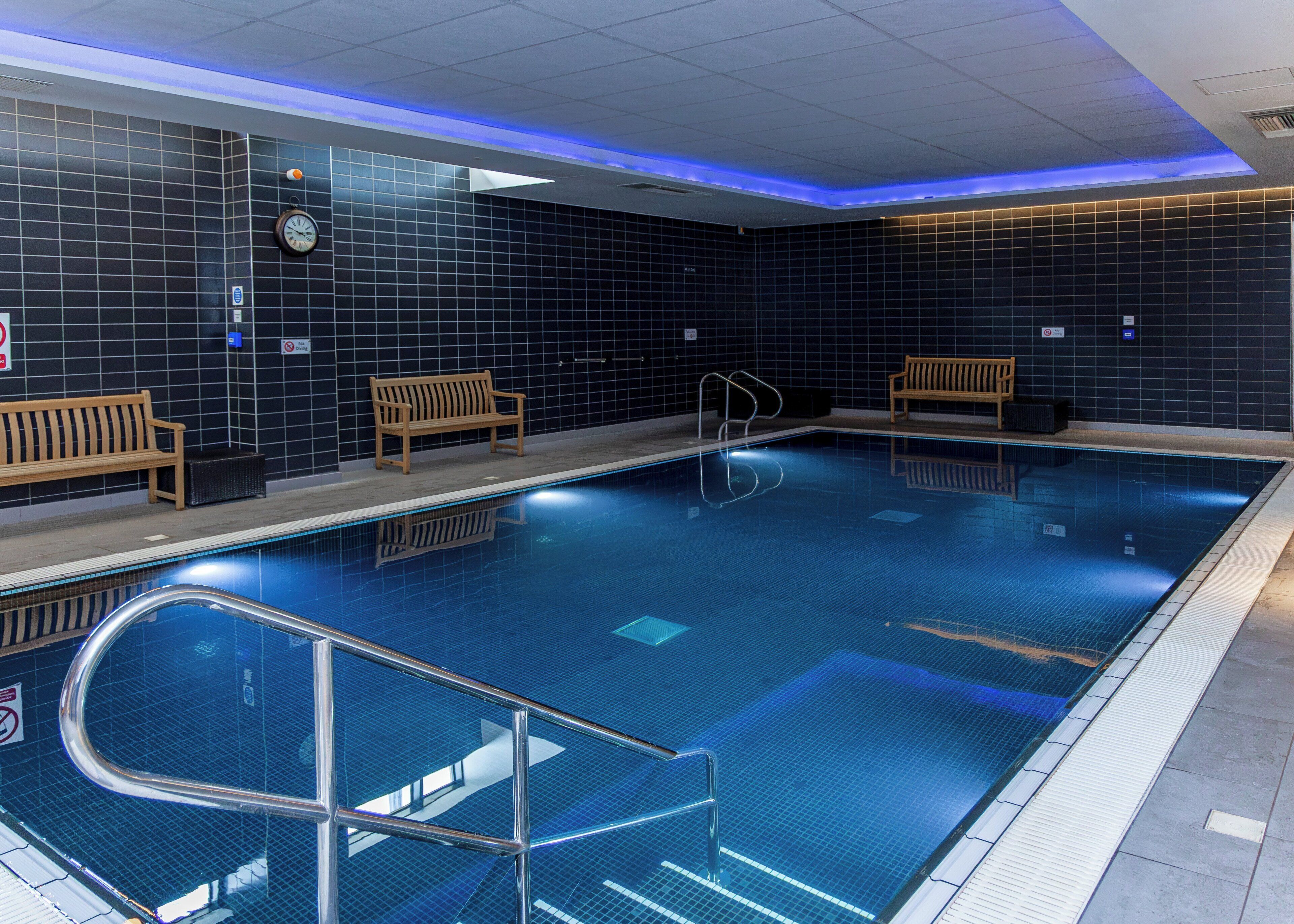 An indoor swimming pool with tiled walls, benches, and a clock.