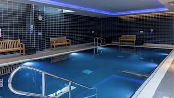 An indoor swimming pool with tiled walls, benches, and a clock.