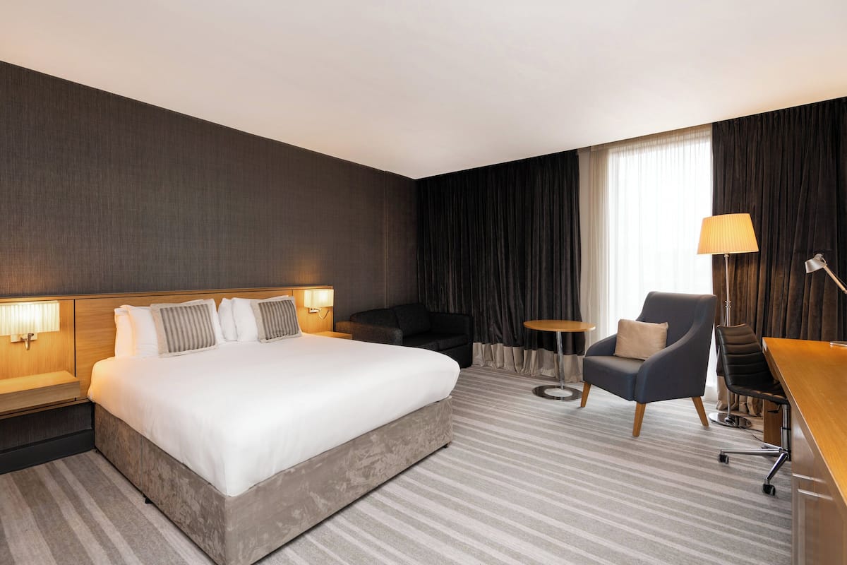 A hotel room with a large bed, a desk, a chair, and a small table.