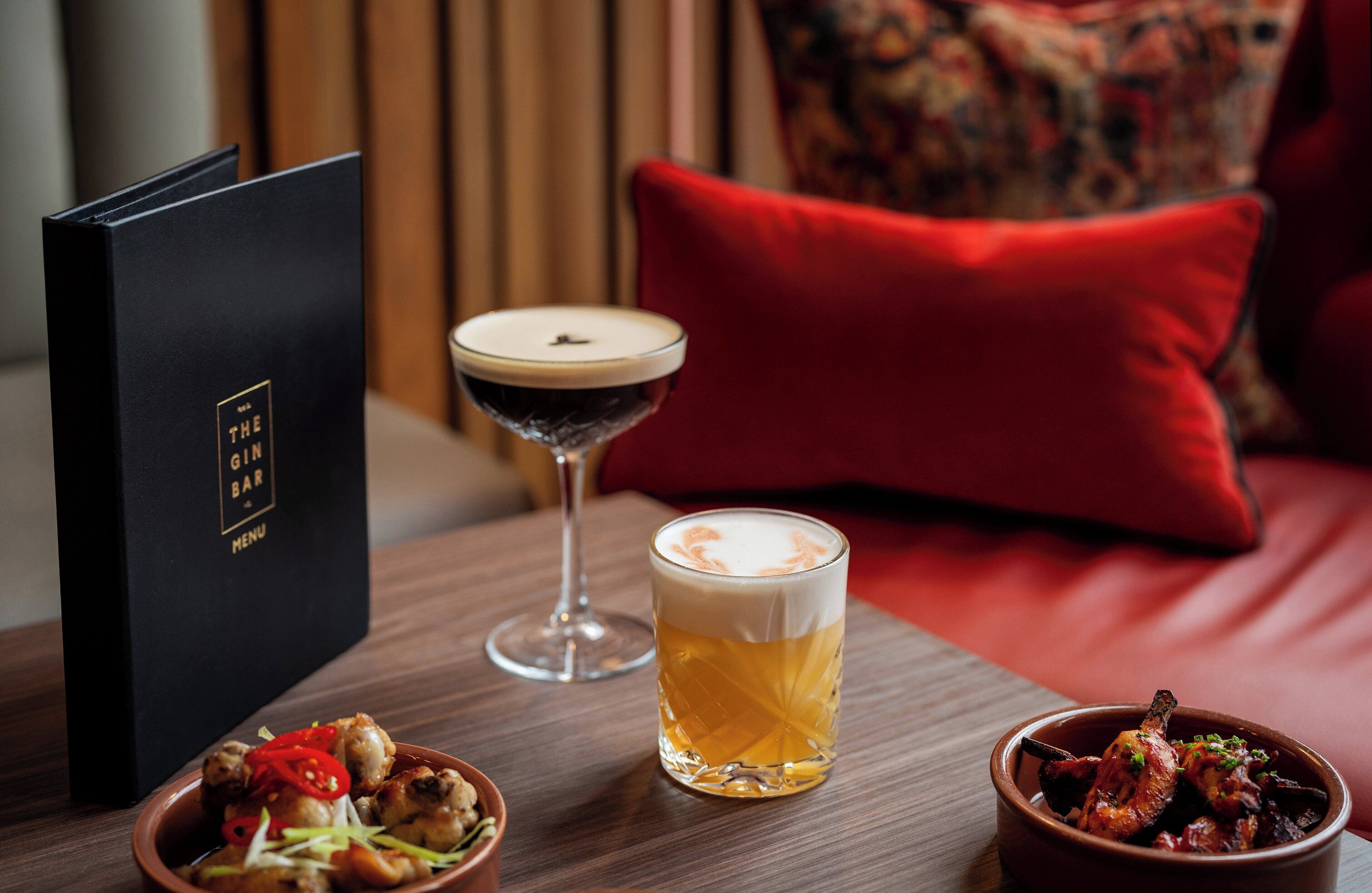 A table with a menu, a martini glass, a beer glass, and a bowl of food.