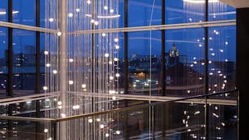 Interior moderno com guarda-corpo de vidro e luminárias pendentes, oferecendo vista para a cidade.