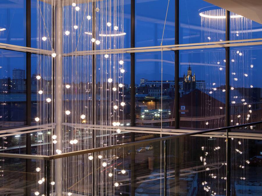 A modern interior with a glass railing and hanging lights, offering a view of the cityscape outside.