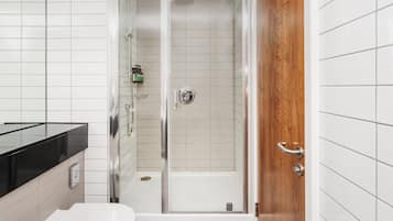 Un baño moderno con ducha de vidrio, puerta de madera y encimera negra.