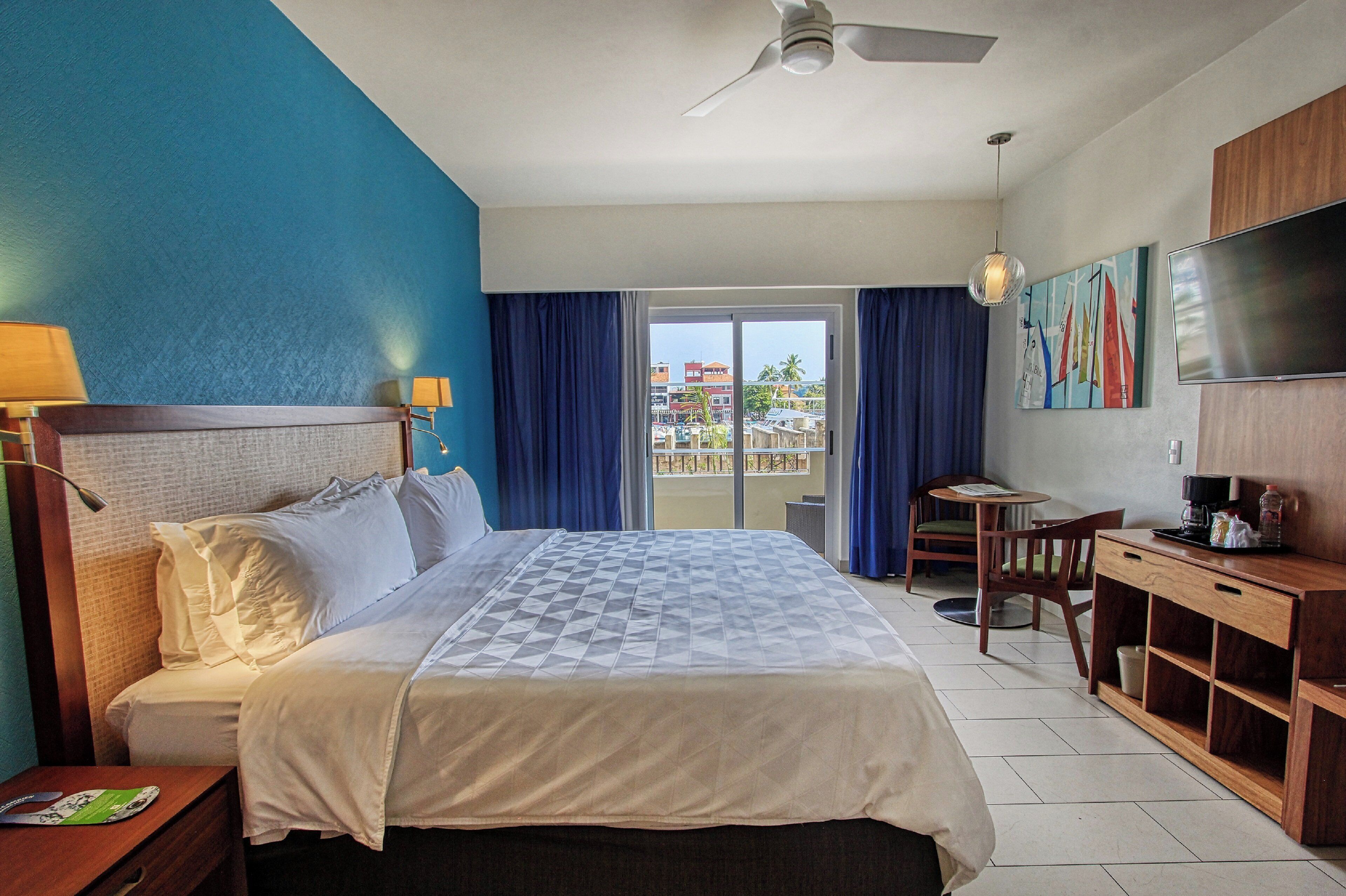A hotel room with a bed, a desk, a chair, a TV, and a balcony with a view.
