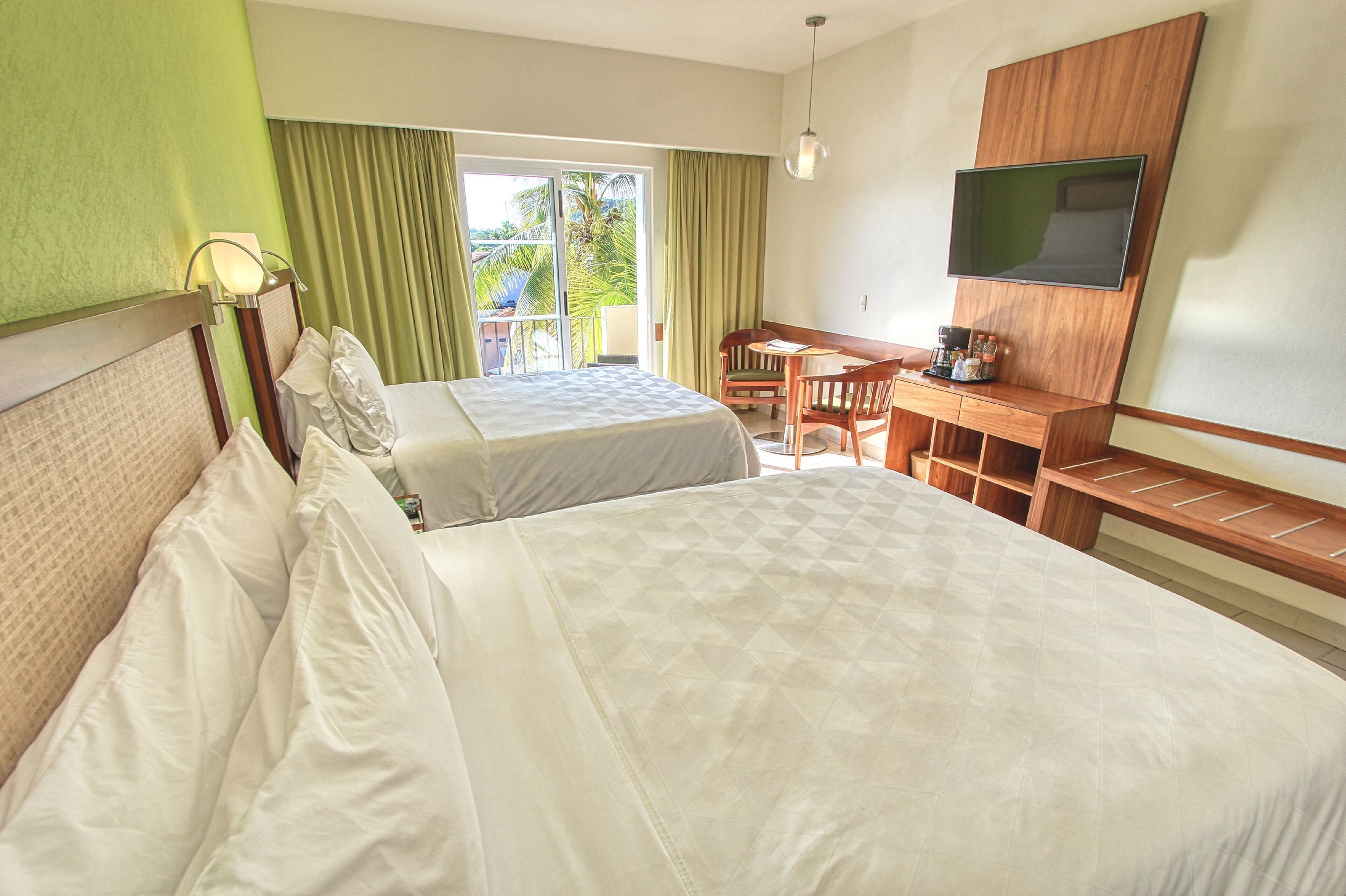 A hotel room with two beds, a desk, a chair, a television, and a balcony with curtains.