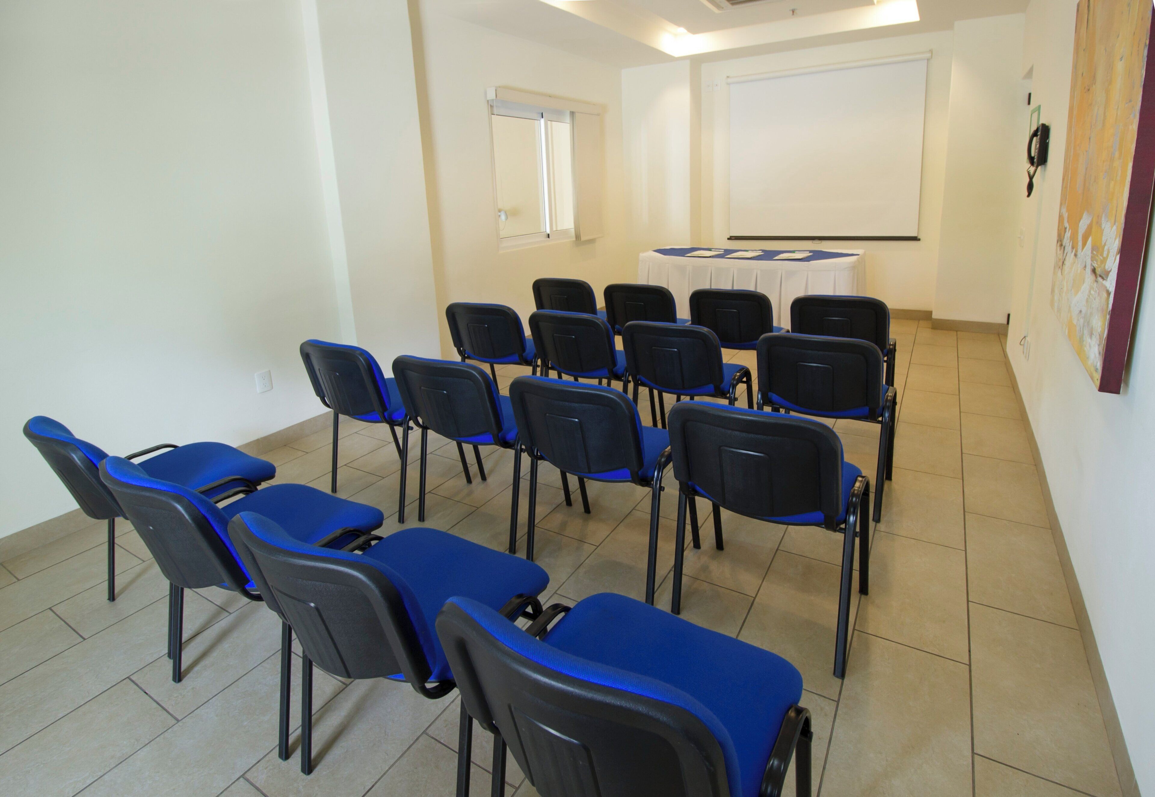 Un salón de conferencias con filas de sillas, una pizarra y una pantalla de proyector.