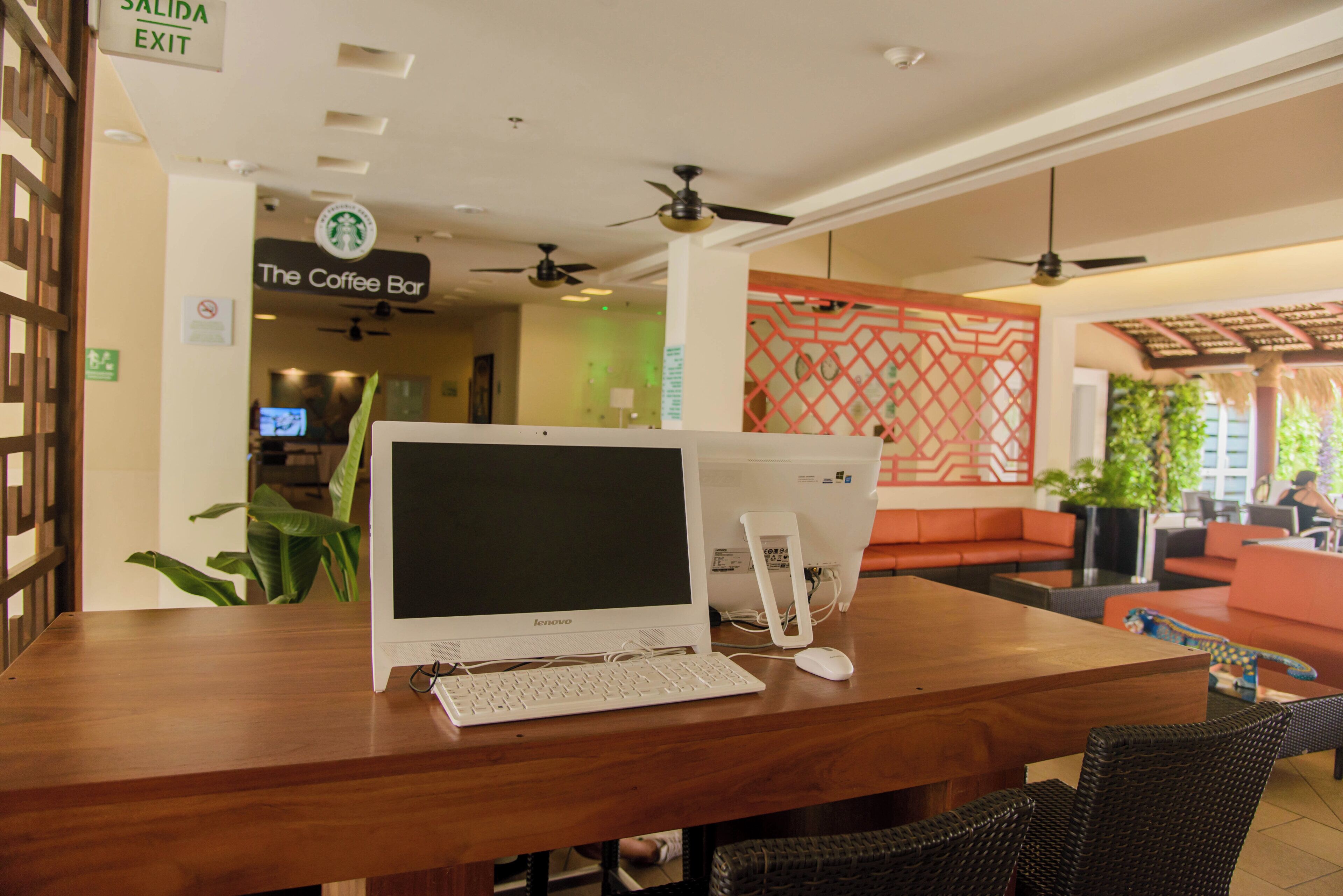 A wooden reception desk with a laptop, a desktop computer, and a mouse. There is a sign for 'The Coffee Bar' in the background.