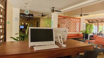 Ein hölzerner Empfangstresen mit einem Laptop, einem Desktop-Computer und einer Maus. Im Hintergrund ist ein Schild für 'The Coffee Bar' zu sehen.