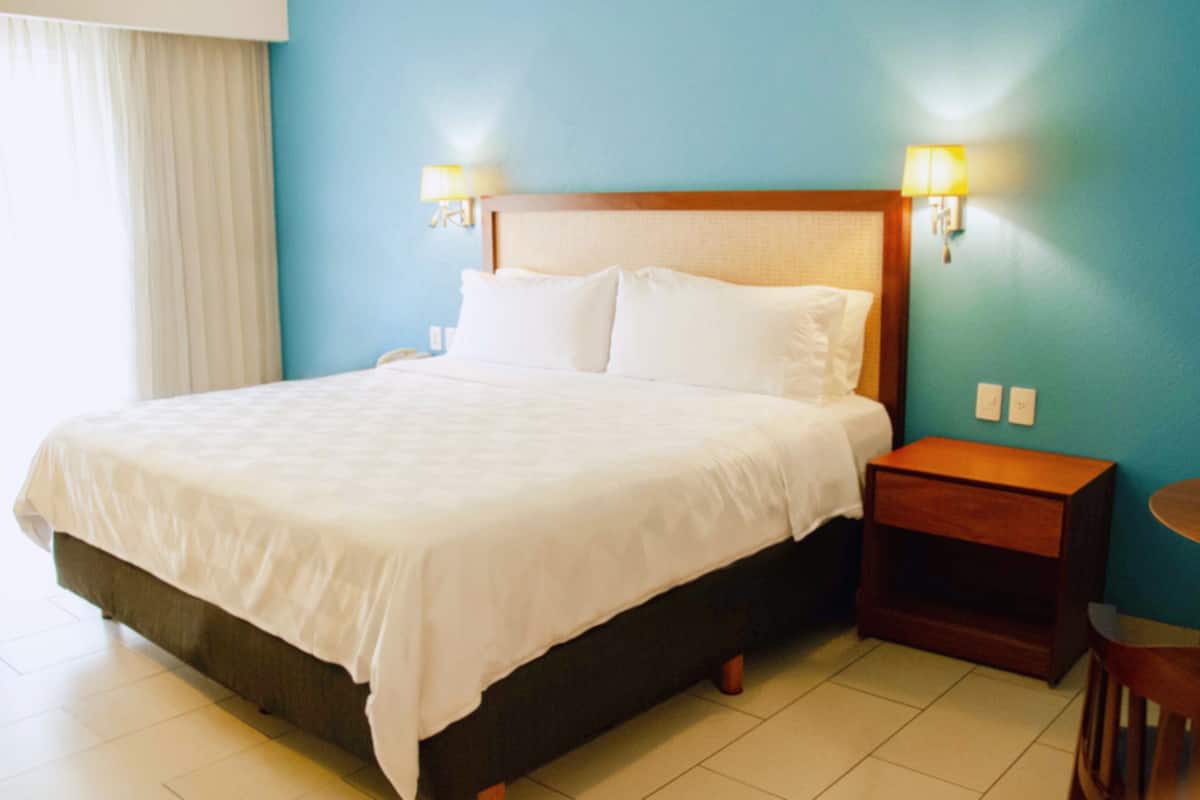A hotel room with a large bed, two bedside lamps, a wooden nightstand, and a small round table.