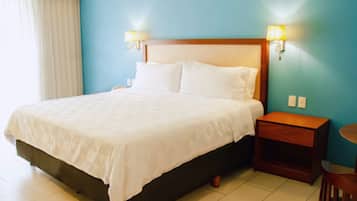 Una habitación de hotel con una cama grande, dos lámparas de noche, una mesita de noche de madera y una pequeña mesa redonda.