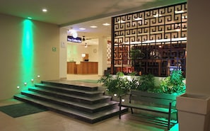 A reception area with a staircase leading to a bar area, a reception desk, and a decorative partition with a geometric pattern. - Holiday Inn Huatulco by IHG (Santa María Huatulco)