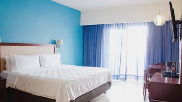 Een hotelkamer met een groot bed, een bureau met stoel, en een raam met blauwe gordijnen.