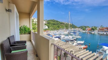 A balcony with wicker furniture, overlooking a marina with boats and buildings in the background.