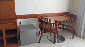 Une pièce de taille modeste, équipée d’un petit réfrigérateur, d’une table en bois et de deux chaises.